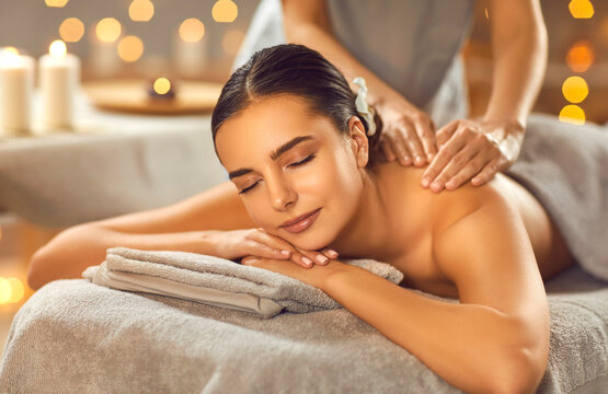 Pretty young woman having massage in spa salon. Close up shot of happy beautiful relaxed woman lying on couch with closed eyes receiving back massage. Beauty treatment, body care