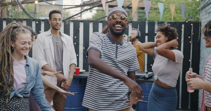 Slow motion portrait of happy African American man student dancing at terrace party enjoying leisure time with friends. Fun and music concept.