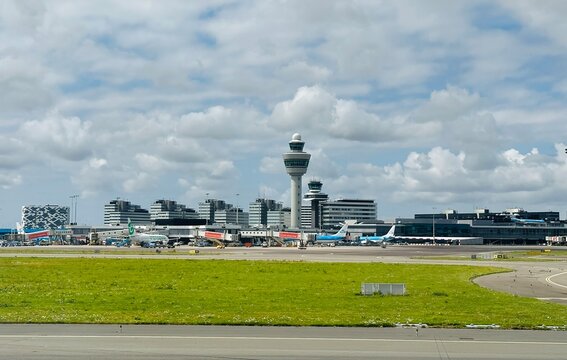 schiphol, netherlands - 23 July 2023: air planes are standing outside the airport terminal with the control tower in the background and departuring airplanes passing by