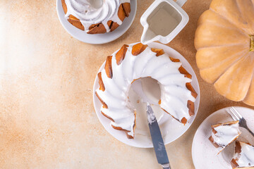 Homemade pumpkin bundt cake. Whole and slices of  sweet pumpkin round sponge cakes topped with sugar or white chocolate glaze icing, beige background copy space