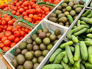 Green cucumbers, avocados, red tomatoes on farmer's food market stall with various organic vegetables.
