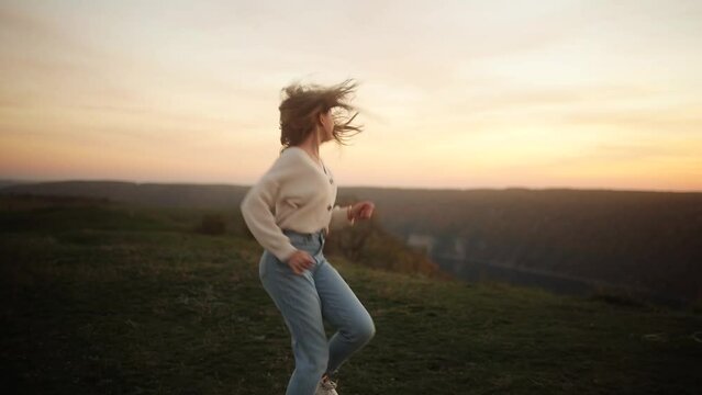 Back view of girl running in the mountains turns around and looking at the camera with incredible pink sunset Happy teenager feeling absolutely free and satisfied outdoors