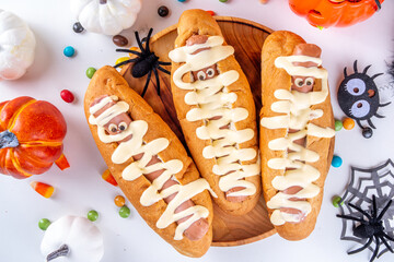Funny mummy hot dogs for Halloween party or kids holiday brunch. Classic hot dogs with cheese eyes and cheesy mayo sauce, with Halloween decor, top view copy space