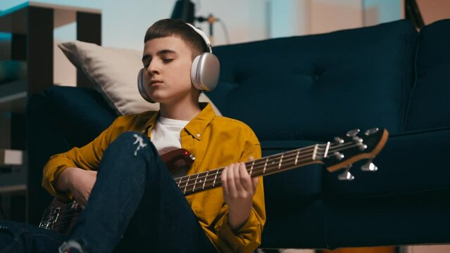 Teen boy wearing headset and enjoying electric bass guitar play at home, hobby