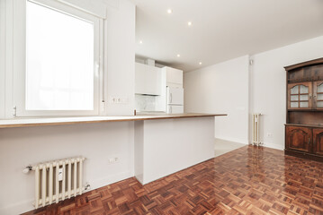 Living room in an apartment with an open kitchen with white furniture and varnished reddish plank parquet floors