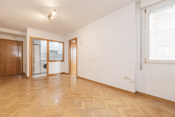 An empty living room in an apartment with a kitchen with a serving hatch window and French oak parquet floors laid in a herringbone pattern