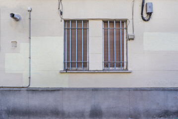 A cement wall with a double window with a gray painted cross grille