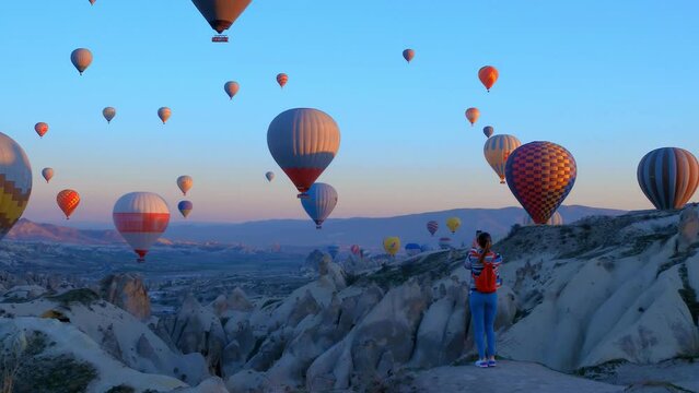 Back view of woman walking at Cappadocia with hot air balloons on a background. 
