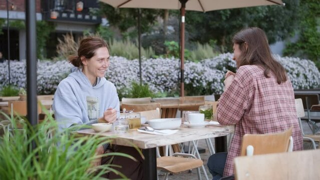 Quality time with friends. Two girls enjoying conversation, their healthy organic vegan acai bowl with fruits. Young woman sharing with her friend over lunch in hipster cafe. Female friendship concept
