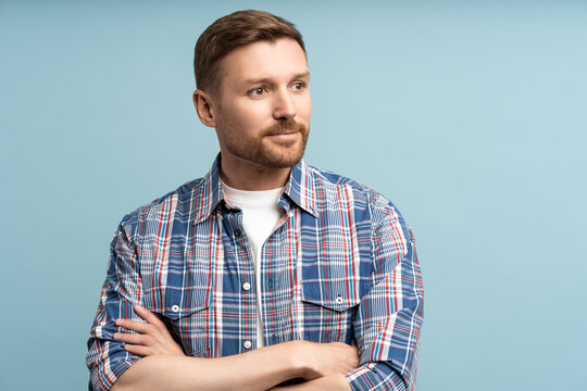 Pensive man isolated on studio wall crossed arms. Satisfied focused guy in plaid shirt smiles quite happily looking away into distance with inspiration. Tranquility, peace, confidence, success concept