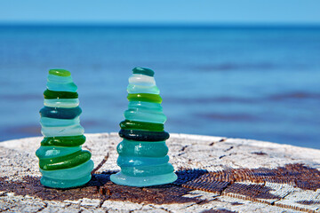 Wet colored glass sea stones arranged in balanced pyramids on a wooden surface against a blue sea background