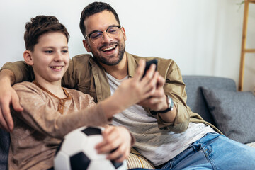 Father and son watching a soccer game while eating popcorn.