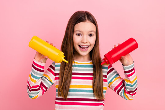 Photo of small funny little girl child joking pouring out mustard red ketchup adding sauces her meal isolated on pink color background
