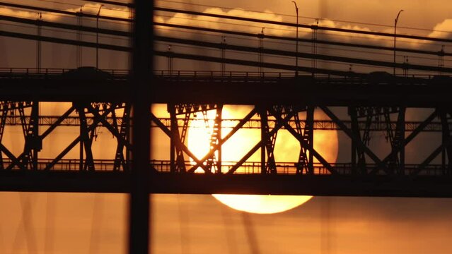 A two-level bridge for electric trains and cars at sunset - a huge bright sun setting down at sunset