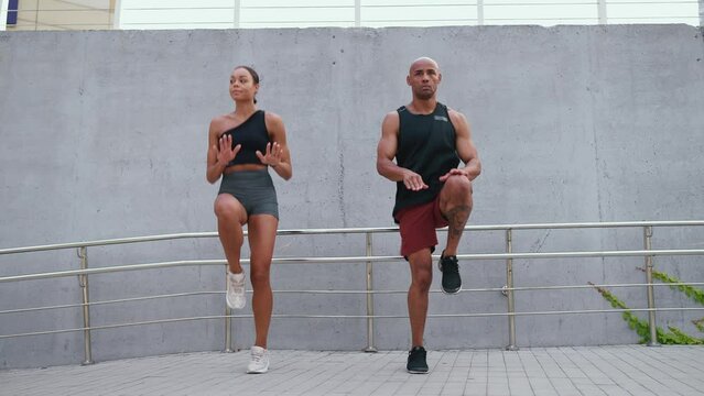 Confident athletic african couple doing jumping jacks on spot near waterfront