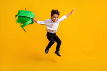 Full length photo of optimistic cute schoolboy wear stylish shirt jumping with backpack in hand...