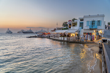 Restaurants and bars along the waterfront of Mykonos town with super yachts in the background - 653840059