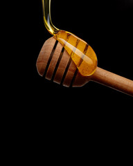 Liquid honey flows onto wooden spoon on black background