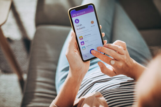 Young woman checking the balance of her bank account on a app on the smartphone on the couch at home
