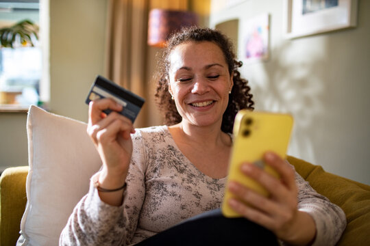 Young mixed woman online shopping from her smartphone on the couch at home