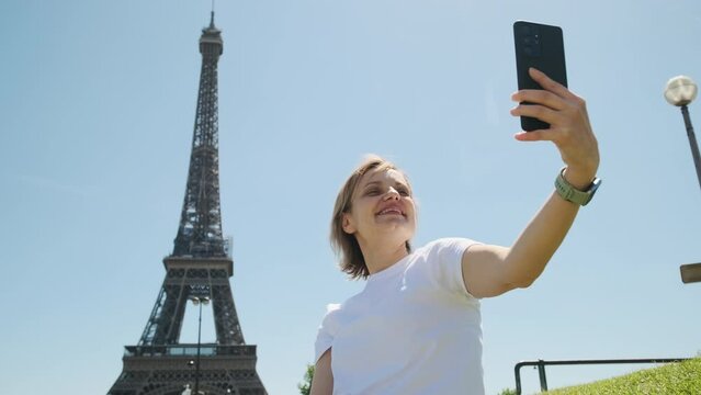 Woman is taking selfie using smartphone sitting near Eiffel tower in Paris in daytime, Close up