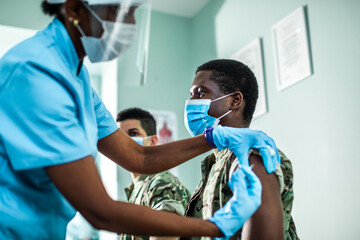 Young army man getting vaccinated by a health worker at the clinic