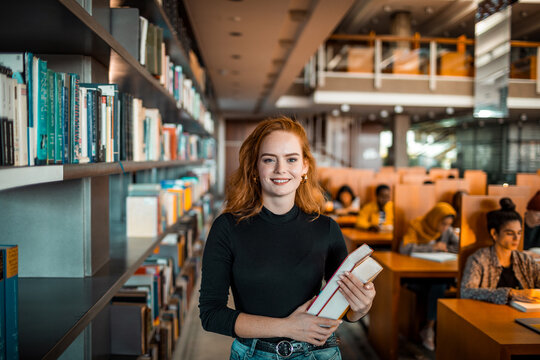 Portrait of a young smart woman holding books in a university library