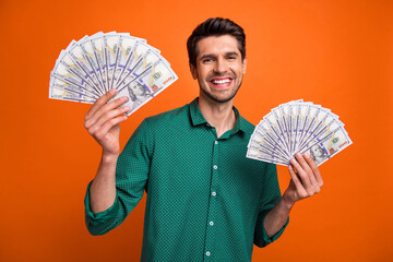 Photo of funky excited man dressed green shirt rising two cash fans isolated orange color background