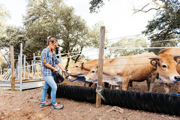 Focused young woman farmer feeding brown cows
