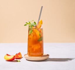 Refreshing peach ice and mint tea. Vegan homemade cold summer drink on tall glass on a light background with fresh fruits and shadows.