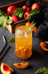 Peach tea with ice and rosemary on a tall glass. Vegan homemade healthy  drink on a dark background with fresh fruits.