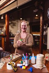 Elderly woman smiling, showing the vase she painted.