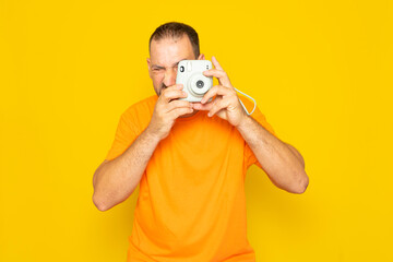 Bearded Hispanic man in his 40s taking a photo with an instant camera, isolated on yellow background.