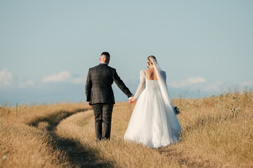 shot of a beautiful bride in a white dress and the groom holding her hand in the middle of a sunny...