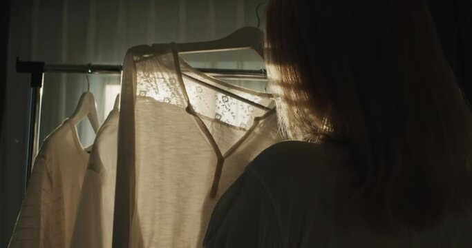 A woman chooses clothes in the dressing room. Silhouette in the sun, rear view