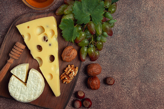 cheese with big holes, emmental, maasdam, brie cheese, on a cutting board, with grapes and honey, nuts, appetizer to wine, top view,