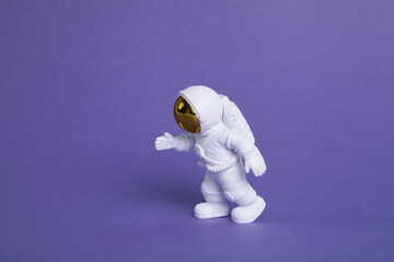 an astronaut figurine in a spacesuit exploring a plain purple background