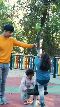 Happy Hispanic parents playing with her children at the synchro spinner in a park. Latin family.