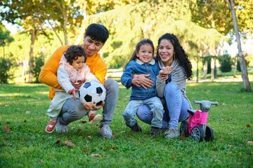 Fototapeta premium Latin family with two children soccer ball and balance bike in a park. Hispanic family.