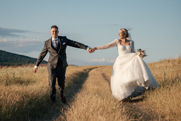 beautiful bride and groom running together, holding hands and being happy, wedding photo shoot in the middle of the meadow, two young people making love, love is in the air, wedding day
