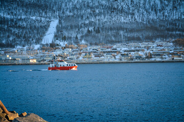 A small red and white ship sails in the Norwegian mountains