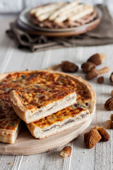 Quiche - open tart pie with morel mushrooms, onion and cheese on wooden cutting board