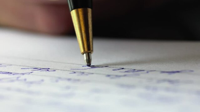 Macro shot of a ballpoint pen. A hand holds the pen and writes a letter or document. Extremely close-up view of the pen and paper with handwriting.