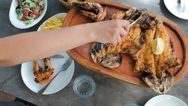 Top view of hand of female putting grilled shrimps on a plate, lunch with seafood at cafe or restaurant