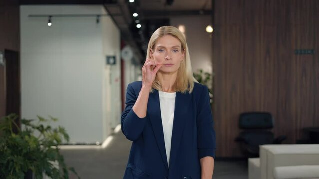 Elegant caucasian woman dressed in formal office outfit closing mouth with imaginary zip and promise to keeping secrets. Faithful attractive woman standing over background of business center.