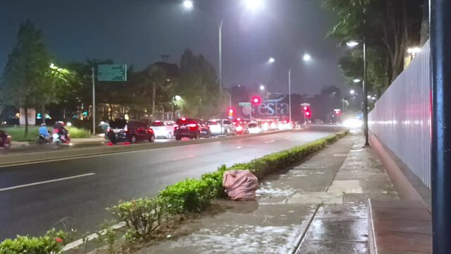 Vehicles at a traffic light on an urban road at night. The queue of vehicles stops when it rains and the traffic light turns red. Rainy season. Low light photography. Street photography.