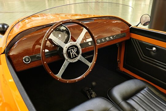 Elegant wooden interior, retro driving wheel and round analogue styled speedometer in microcar two seated microcar Patak Rodster made by Slovak company Patak Motors, displayed on car expo in Nitra.