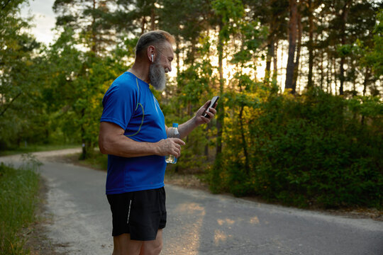 Retired man jogger taking break drinking water watching funny video on phone