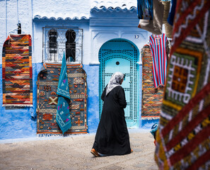 silhouette of a local woman passing the colorful blue wall and carpets on the streets of Chefchaouen Morocco