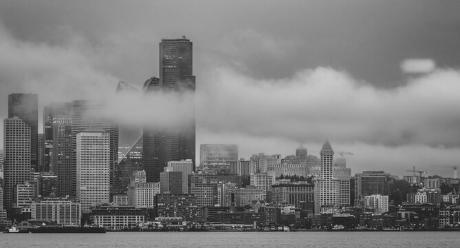 Seattle skyline form West Seattle across Elliott Bay on a rainy afternoon with wisps of low clouds and fog drifting through the tall buildings; Seattle, Washington, United States of America